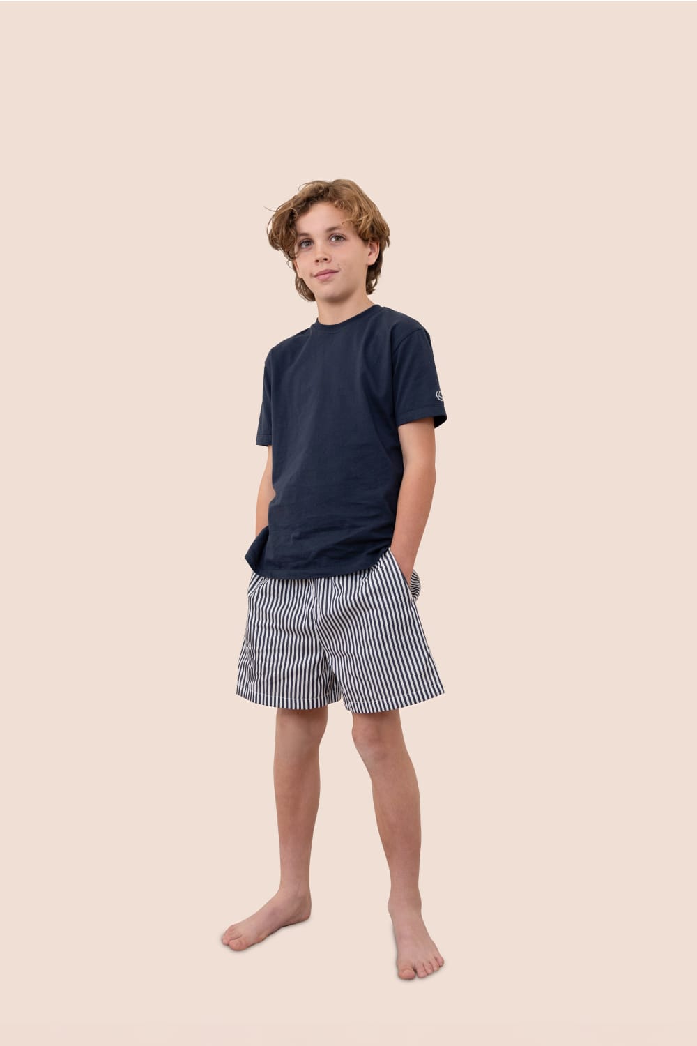 Young boy wearing a navy t-shirt and striped shorts on a beige background