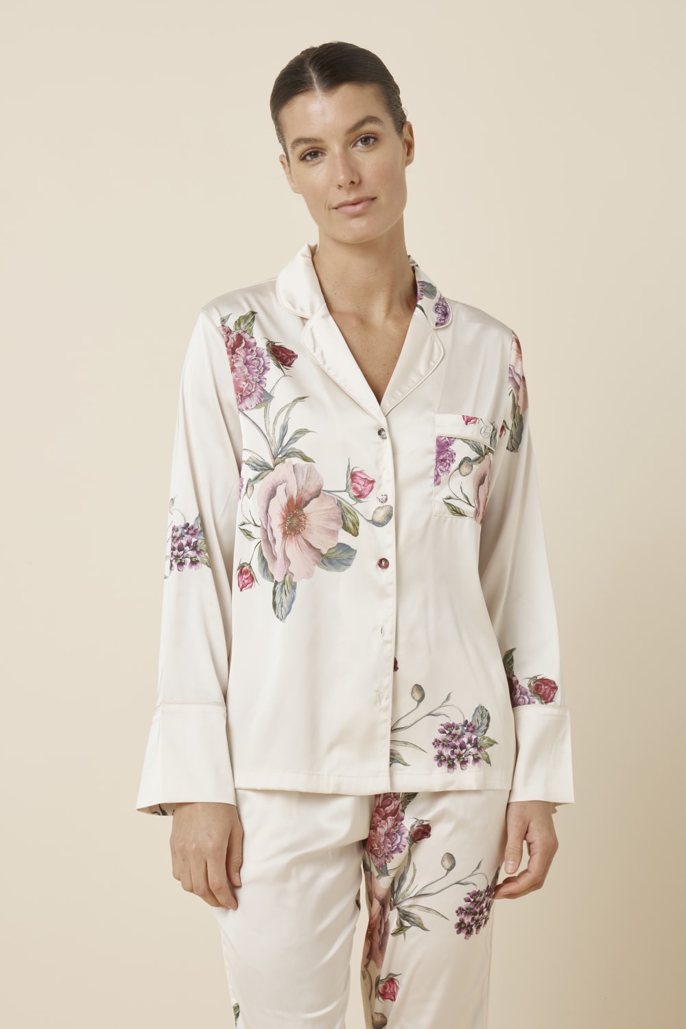 Woman wearing a Ruby Floral Satin PJ set Ivory colour, close up view of top with floral patterns on a beige background
