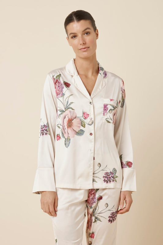 Woman wearing a Ruby Floral Satin PJ set Ivory colour, close up view of top with floral patterns on a beige background