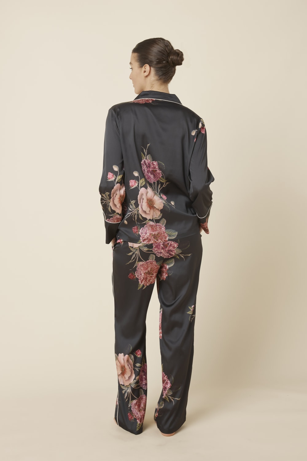 Woman wearing a Ruby Floral Satin PJ set in black with a beige background back shot. 