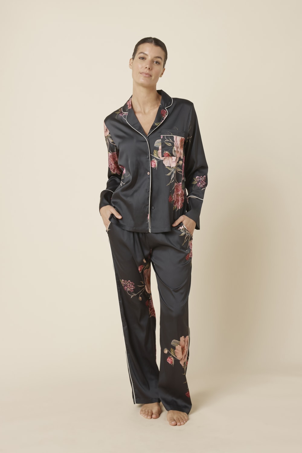 Woman wearing a Ruby Floral Satin PJ set black front view with floral patterns on a beige background