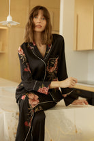 Woman wearing a Ruby Floral Satin PJ set black sitting on a marble bench.