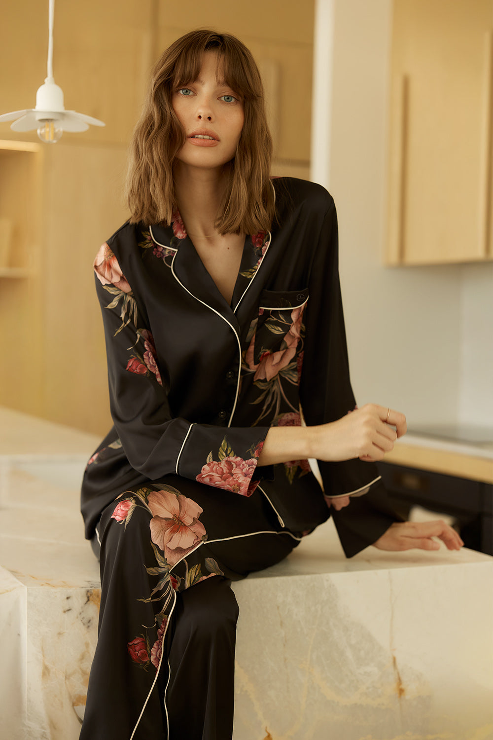Woman wearing a Ruby Floral Satin PJ set black sitting on a marble bench.