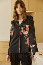 Woman wearing a Ruby Floral Satin PJ set in black with a room with wooden closet behind.