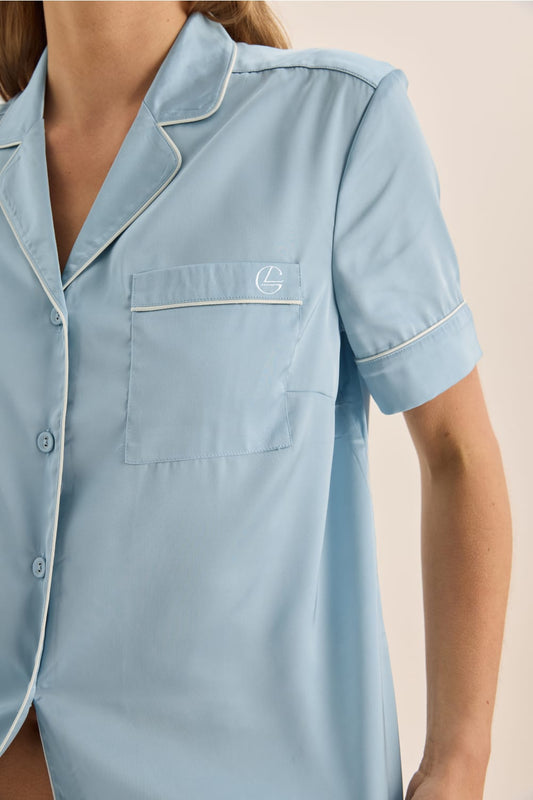Light blue pajama top with a logo on the chest pocket against a beige background