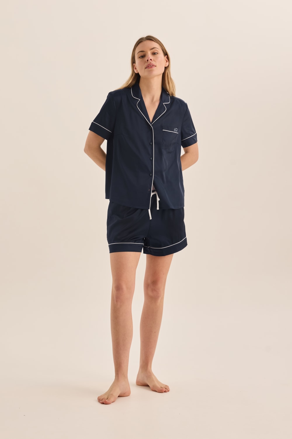 Woman wearing navy pajama set with white piping on a beige background