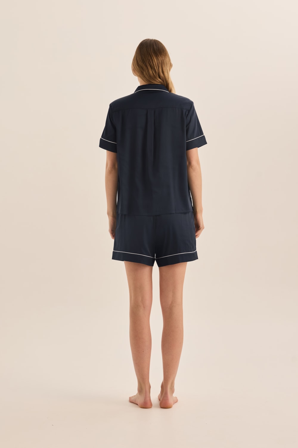 Person wearing navy blue pajama set with white trim on a beige background