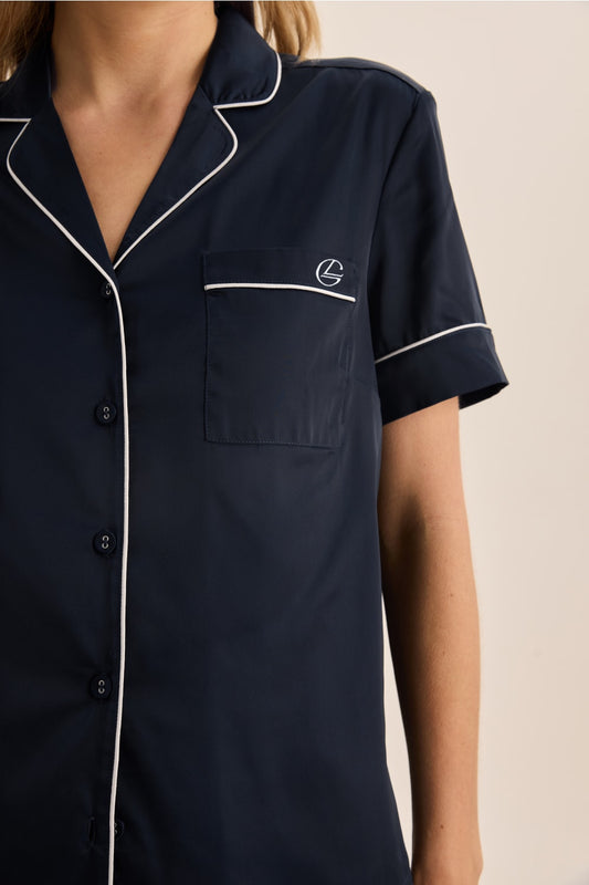 Navy blue pajama top with white piping and logo on a beige background