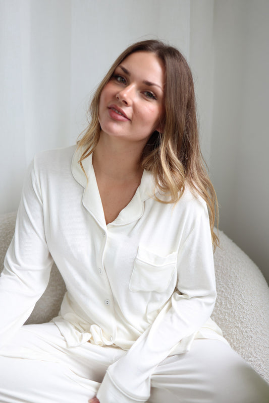 Woman wearing a white outfit sitting on a white surface with a neutral background