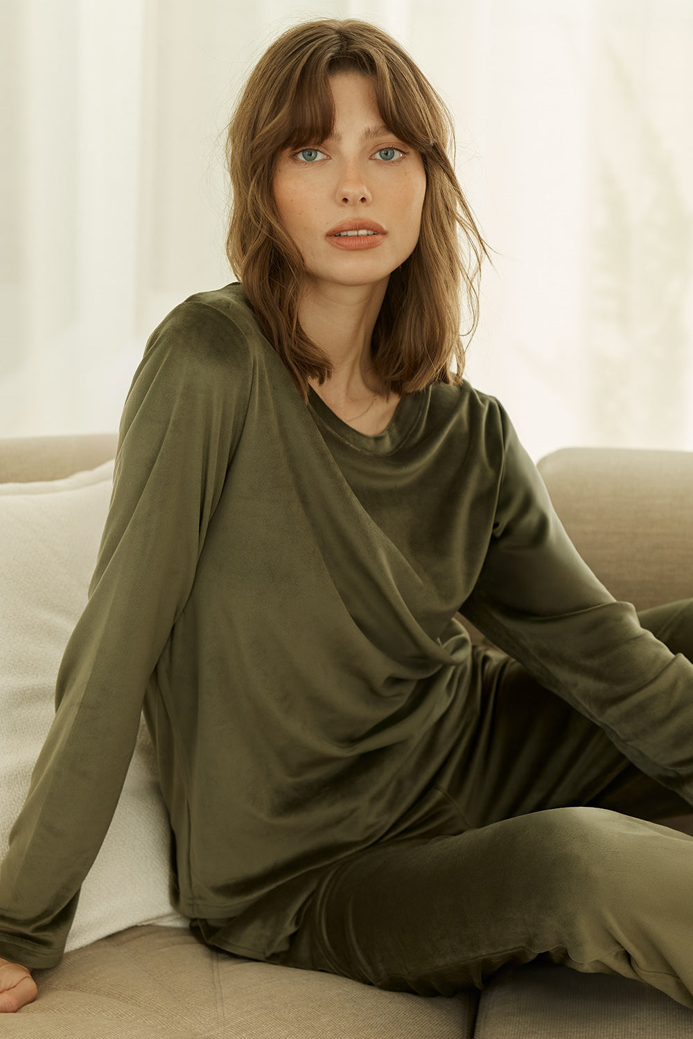 Thea Velour Long Lounge Set Olive shown on model seated, featuring a soft draped long sleeve top and relaxed wide leg lounge pants in olive green velour fabric.