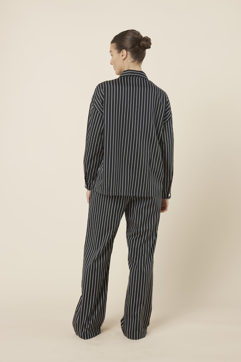 Woman wearing a black and white striped willow cotton stripe pyjama PJ set in set on a beige background and back view