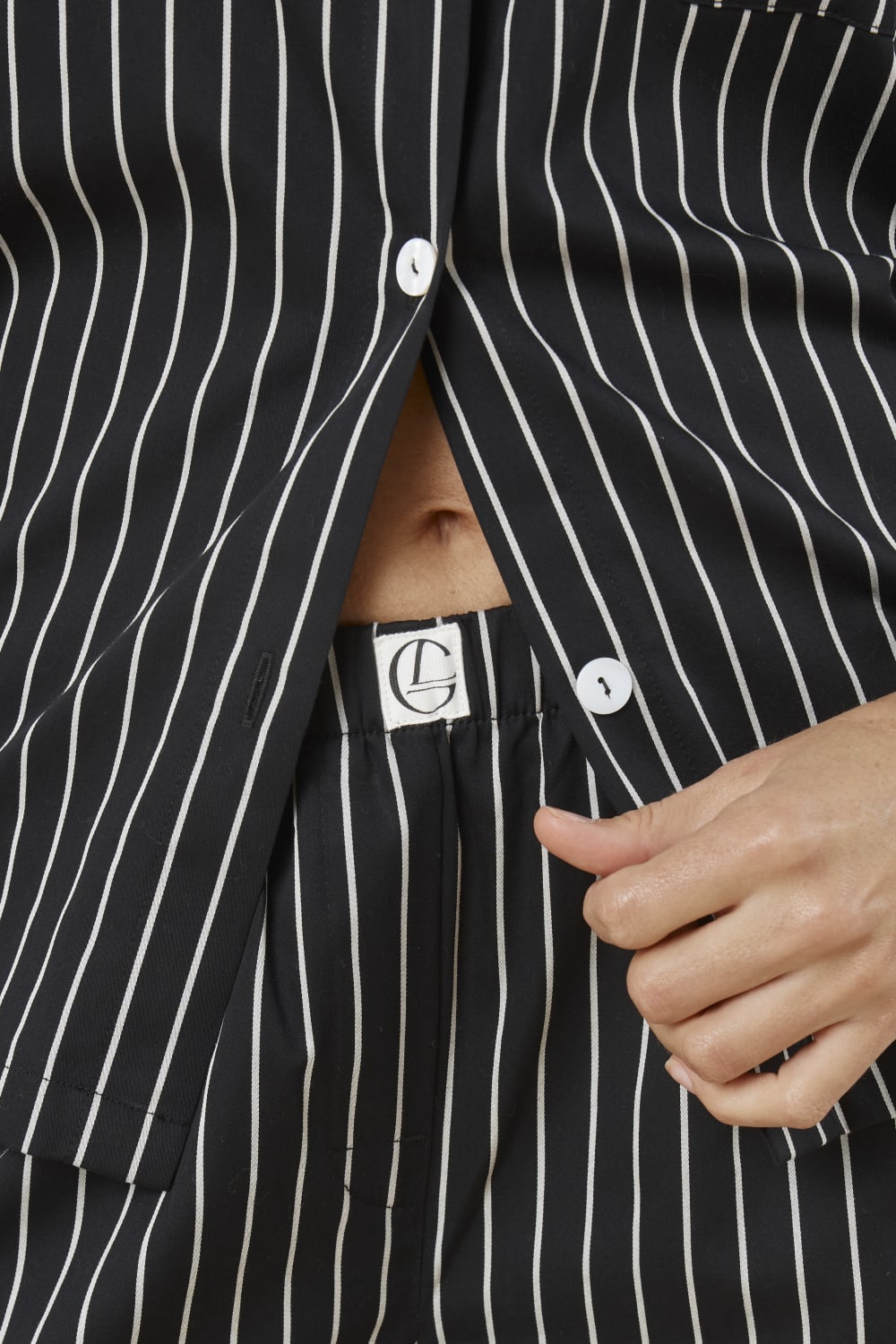 Close up of top of a woman wearing a black and white pin striped willow cotton stripe pyjama PJ set showing the waistline and gingerlilly embroidery with white buttons