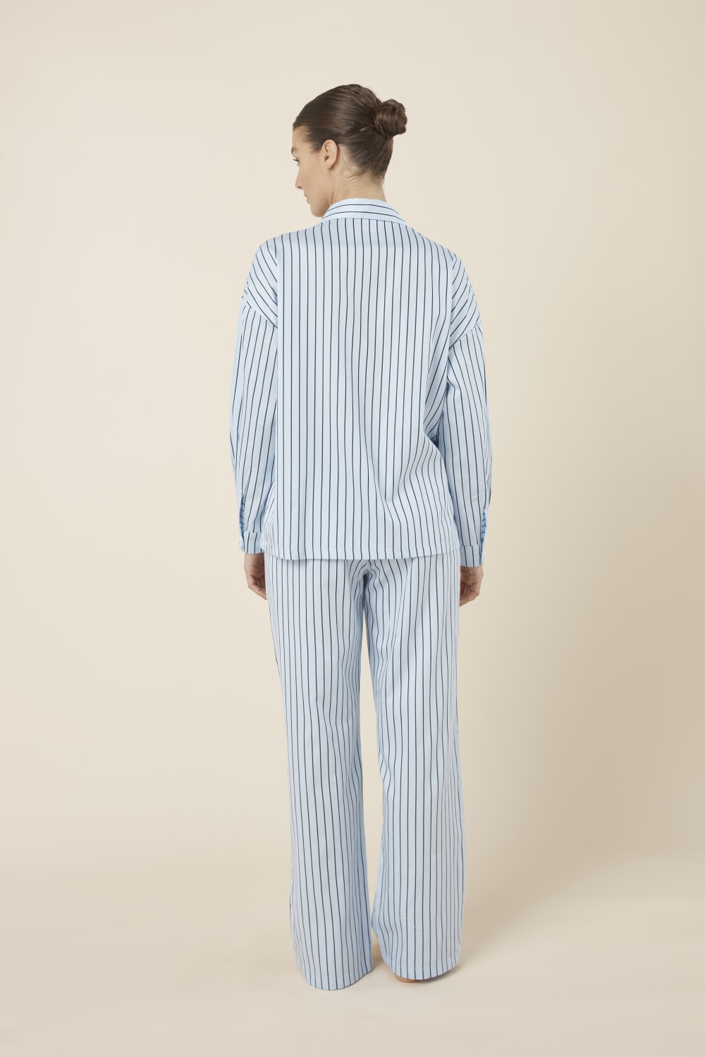 Woman wearing a blue striped willow cotton stripe pyjama PJ set on a beige background and back view