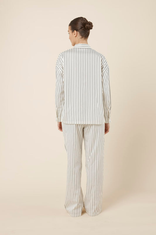 Woman wearing a black and white striped ivory willow cotton stripe pyjama PJ set in set on a beige background back view
