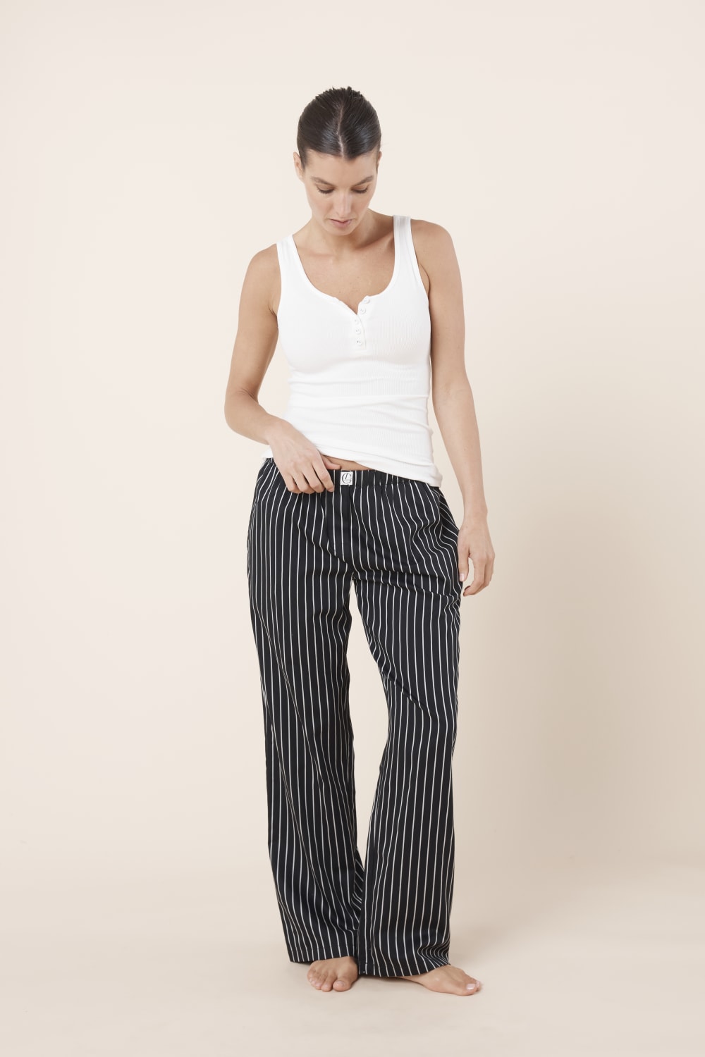 Woman wearing a white tank top and Willow Cotton Striped Pant in Black and white on a beige background