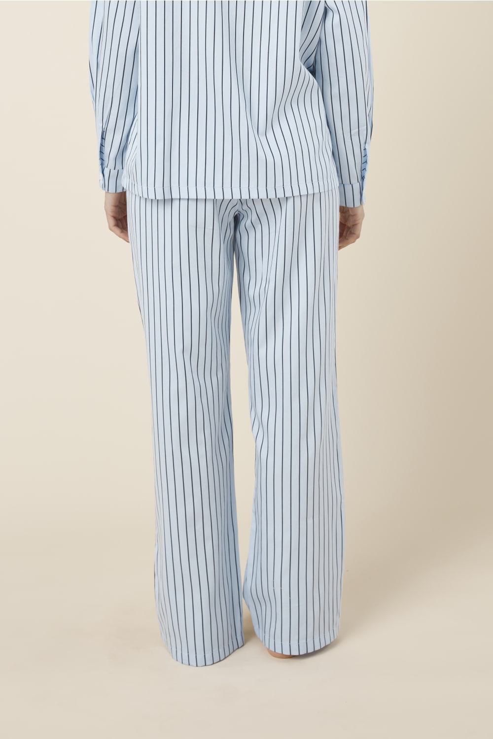 Person back view wearing the willow cotton striped pant in blue and white on a beige background.