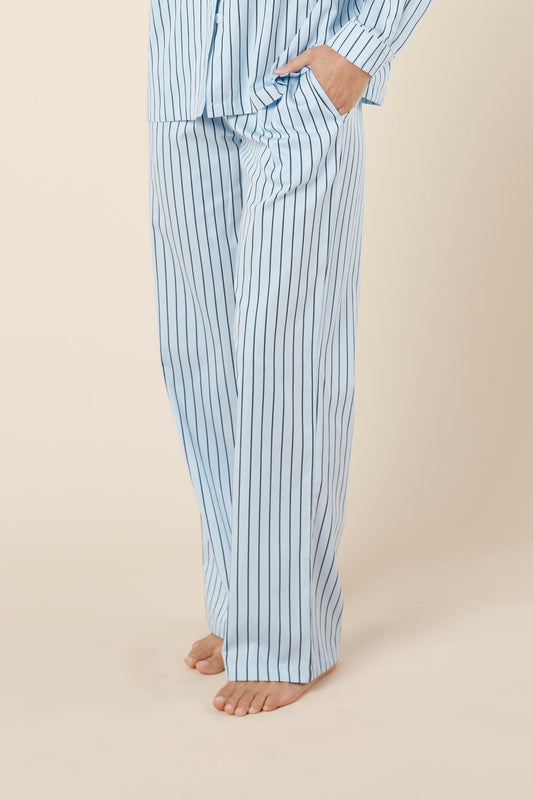 Person wearing willow cotton striped pyjama pants in blue on a beige background side view. 