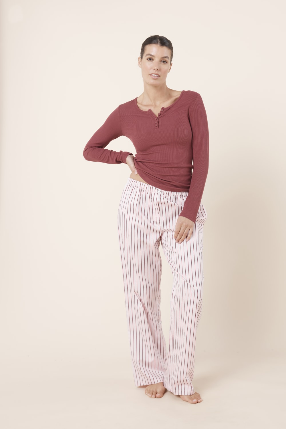 Woman wearing a mauve long-sleeve top and Willow Cotton Striped Pant in Pink and white stripe on a beige background