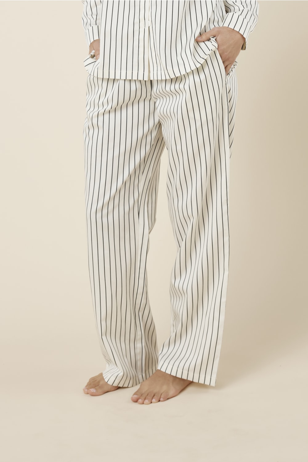 Woman wearing black and white striped willow cotton striped pyjama pj set in ivory on a beige background side view.