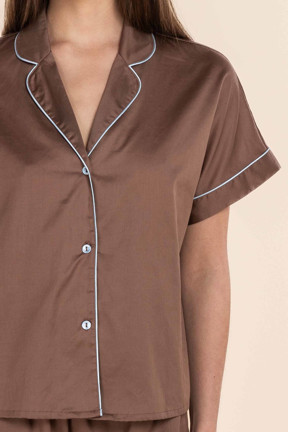 Brown pyjama top with blue piping on a beige background