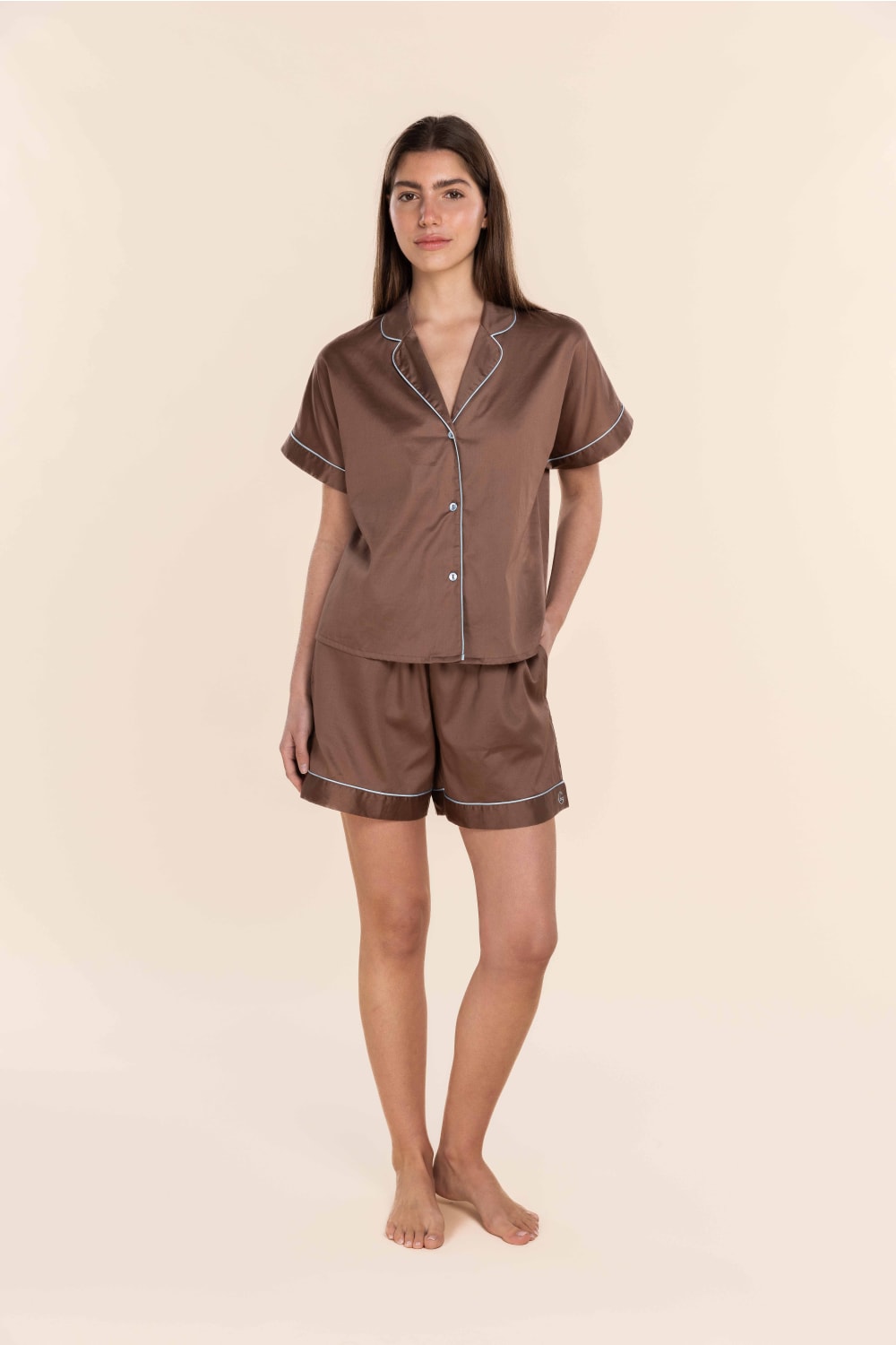 Woman wearing a brown satin pyjama set against a beige background