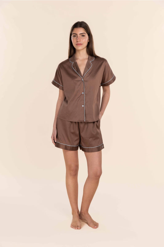 Woman wearing a brown satin pyjama set against a beige background