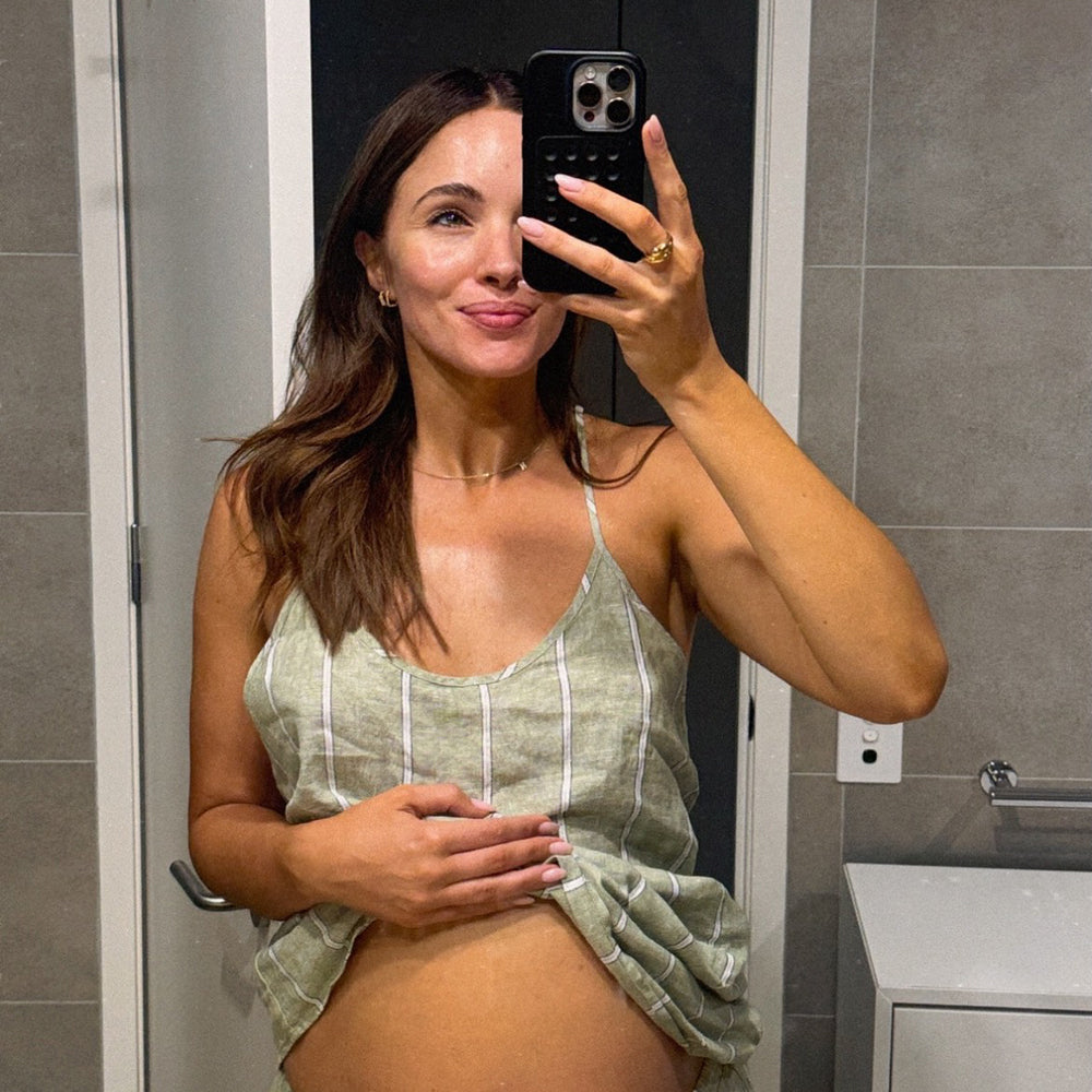 Woman taking a mirror selfie in a bathroom wearing a green and white striped dress.