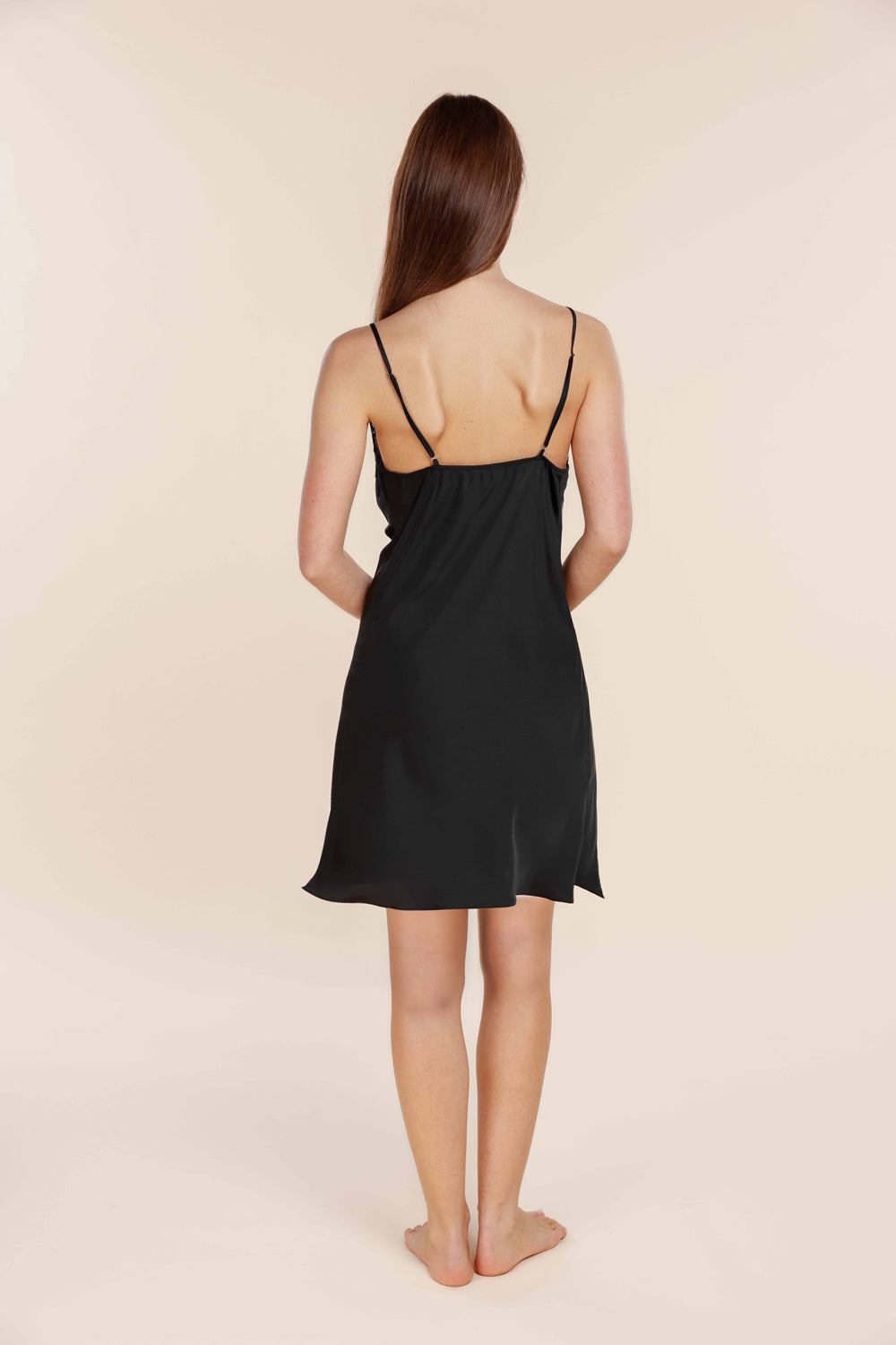 Woman wearing a black slip dress against a beige background