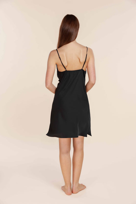 Woman wearing a black slip dress against a beige background