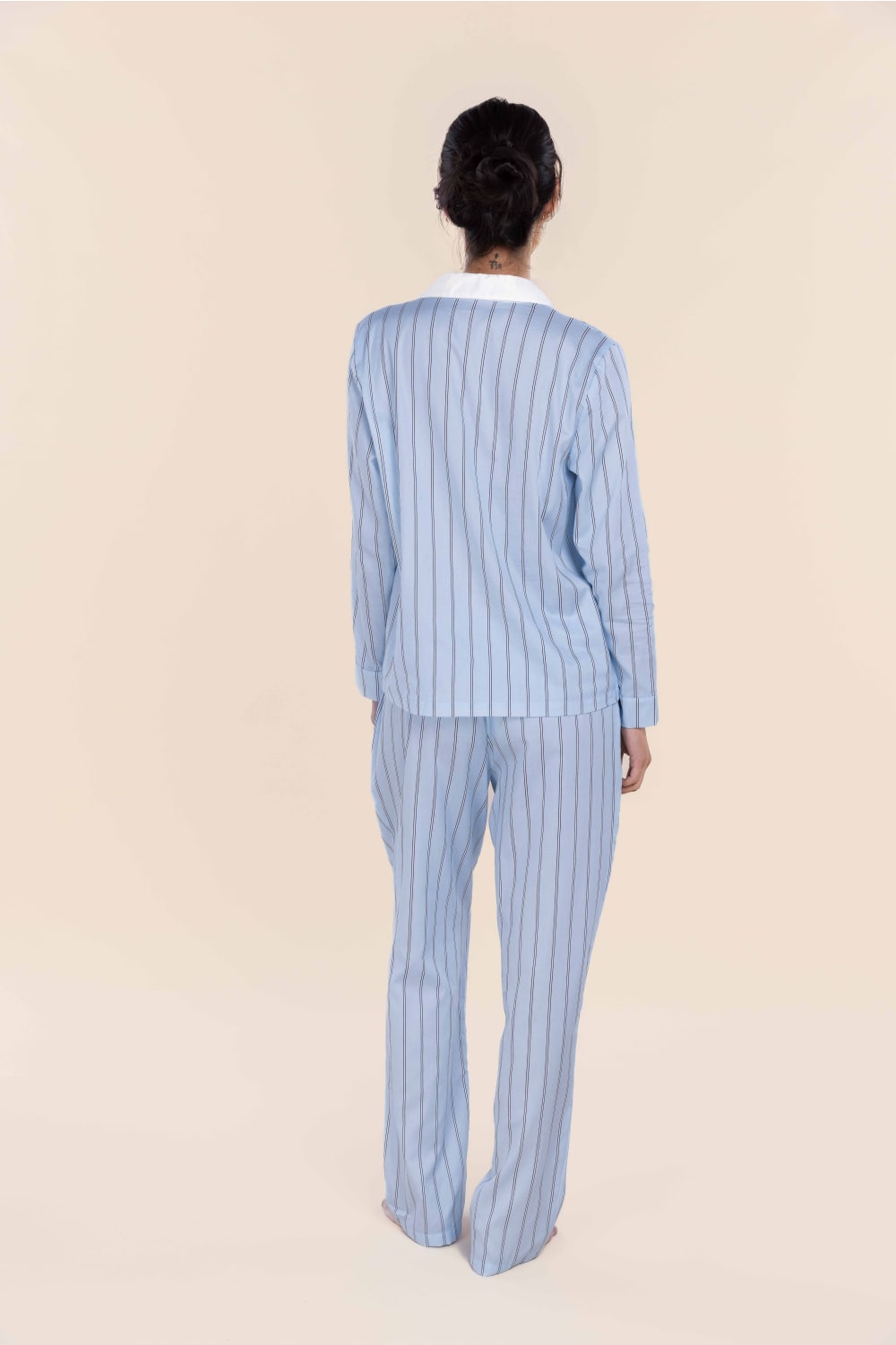 Person wearing a light blue pinstripe pajama set on a beige background
