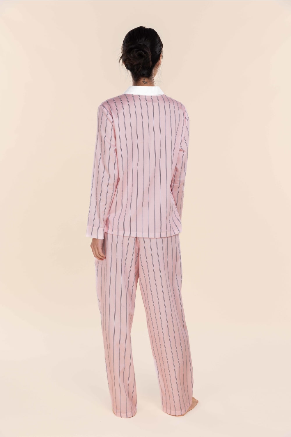 Person wearing a pink and white striped pajama set on a beige background