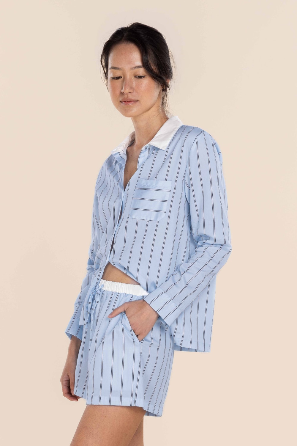 Woman wearing a light blue striped pajama set on a beige background