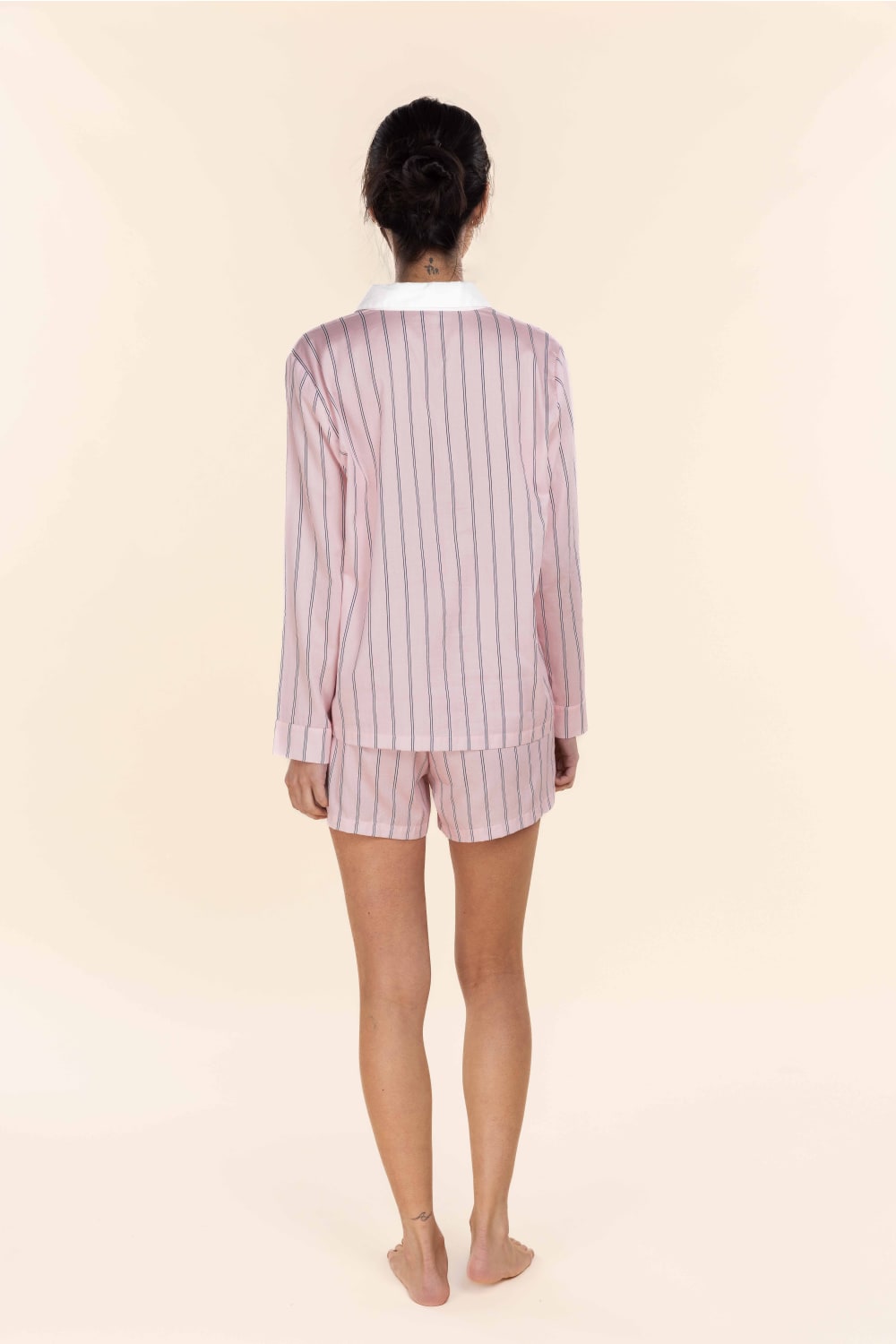 Person wearing a pink and white striped pajama set on a beige background