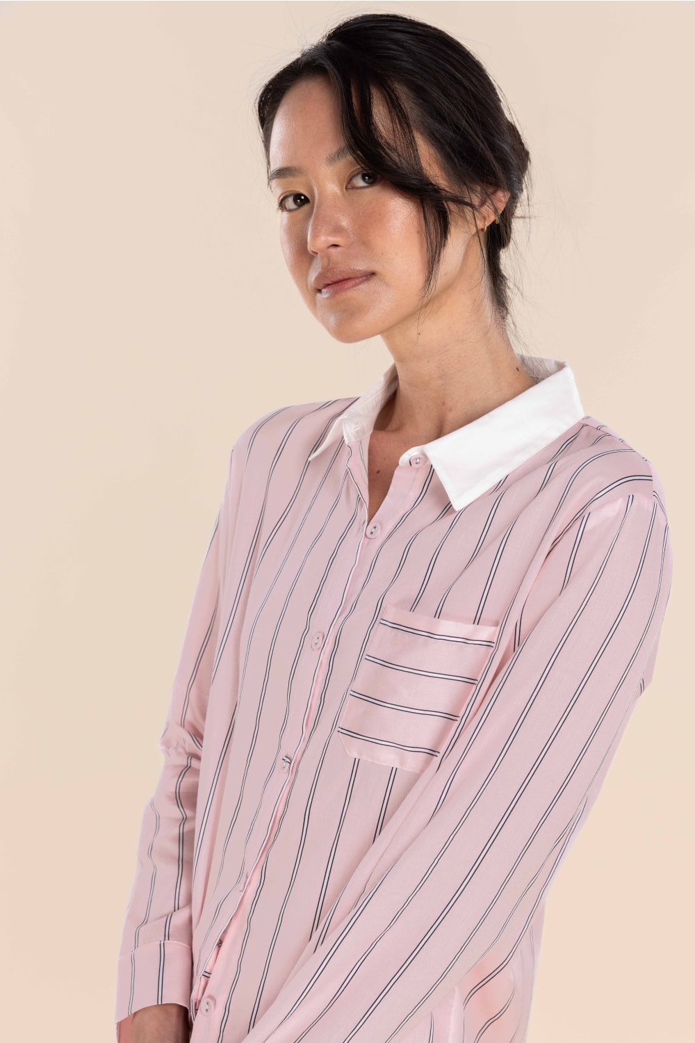 Woman wearing a pink striped shirt with a white collar against a beige background