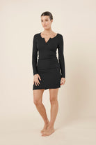Woman wearing a black bonnie ribbed long sleeve midi henley nightdress against a beige background side on view