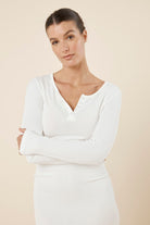 Woman wearing a ecru ivory white bonnie ribbed long sleeve midi henley nightdress against a beige background close up of upper body