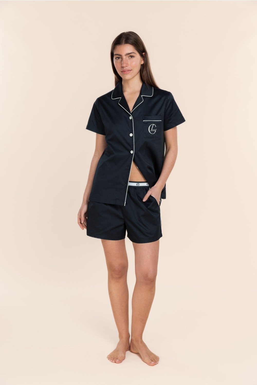 Woman wearing a navy pajama set with a logo on a beige background