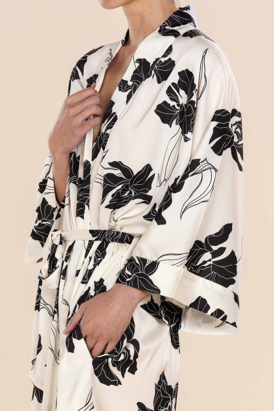 White robe with black floral pattern worn by a person on a beige background