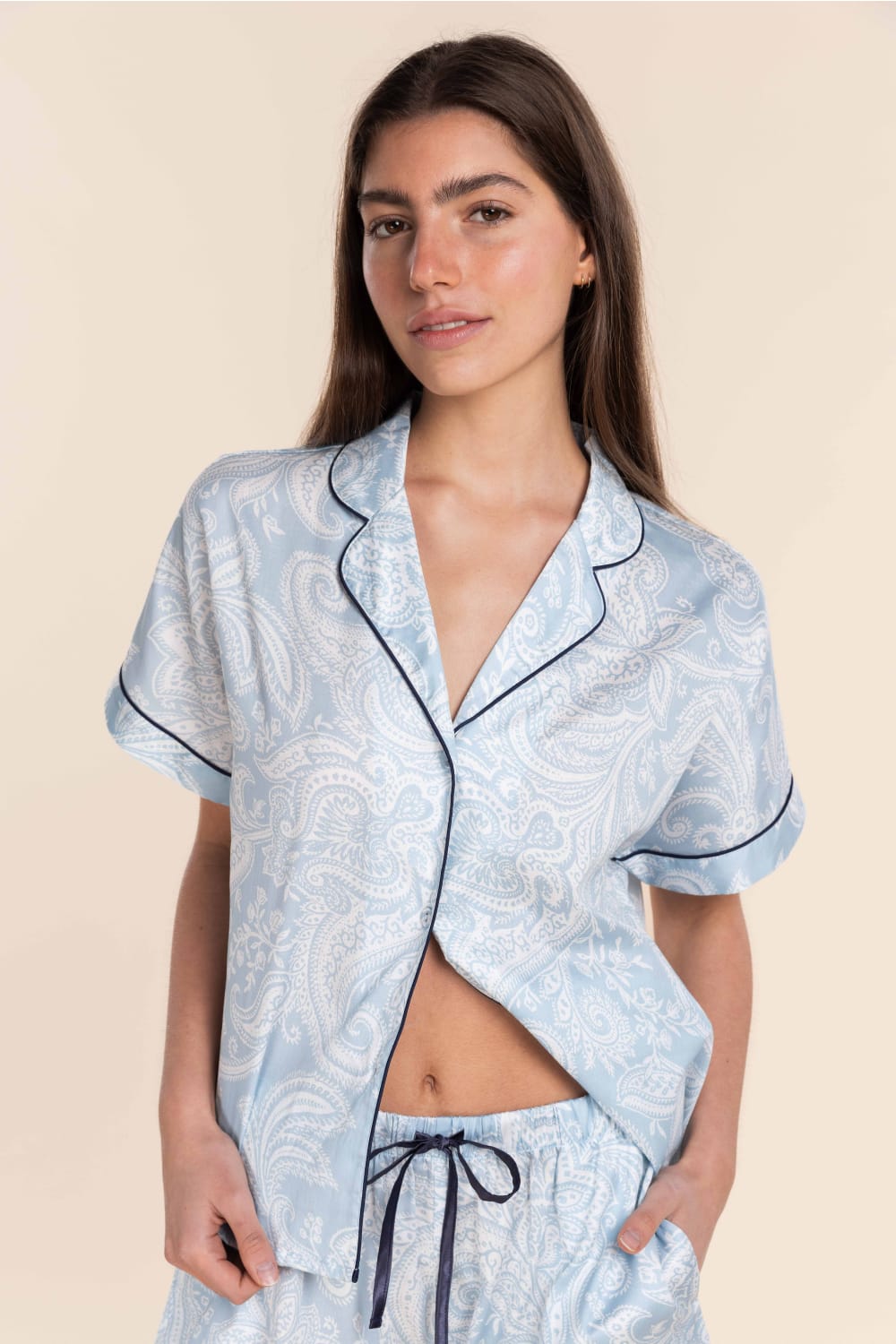 Woman wearing a light blue pajama set with a pattern on a beige background