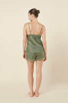 Woman back side view wearing a green olive heather silky satin cami and short set with lace detail on a beige background