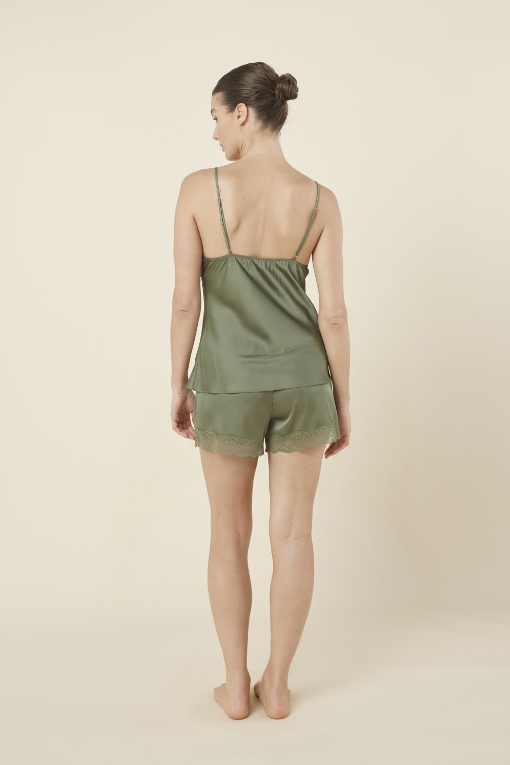 Woman back side view wearing a green olive heather silky satin cami and short set with lace detail on a beige background