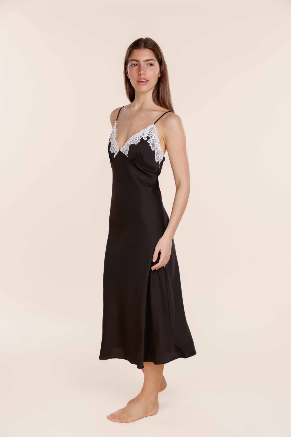 Woman wearing a black slip dress with lace trim on a beige background