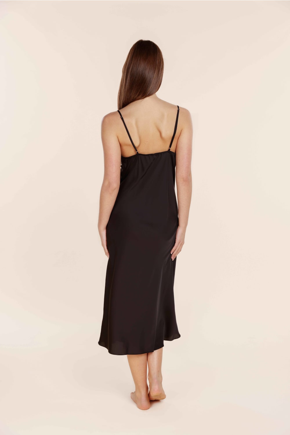 Woman wearing a black slip dress on a beige background