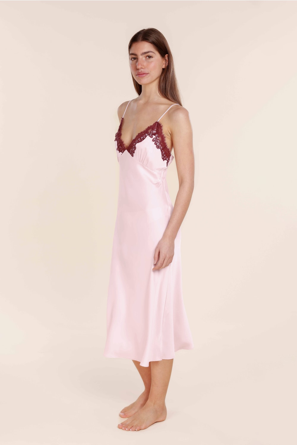 Woman wearing a pink satin nightgown with lace trim on a beige background