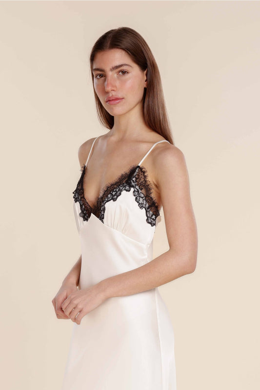 Woman wearing a white slip dress with black lace details on a beige background