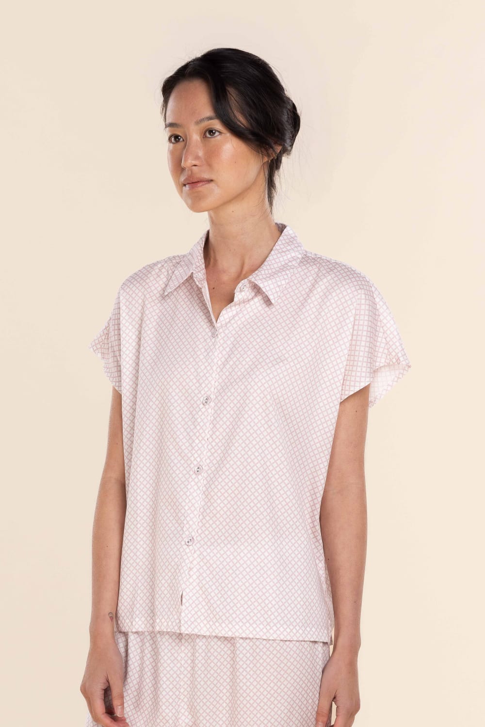 Woman wearing a short-sleeve patterned shirt against a beige background