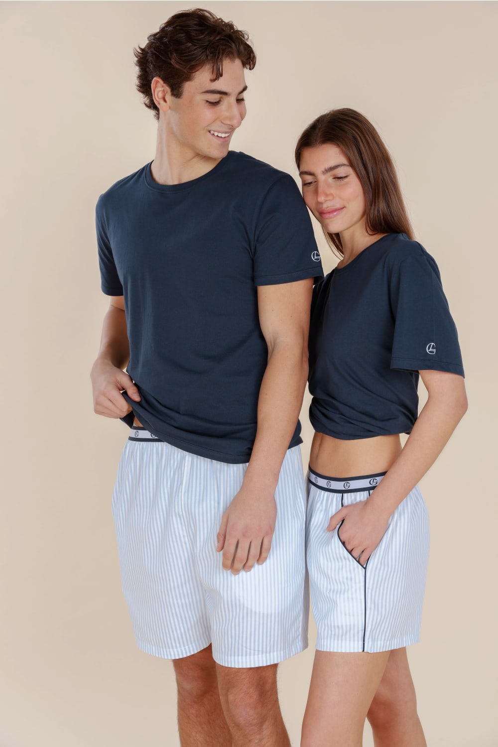 Two people wearing matching navy t-shirts and light blue shorts on a beige background