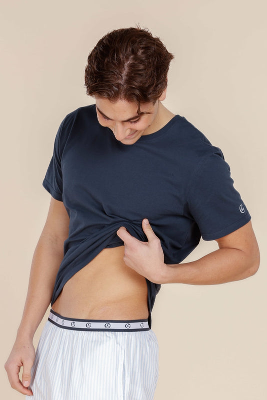 Person wearing a navy blue t-shirt with a brand logo, standing against a beige background