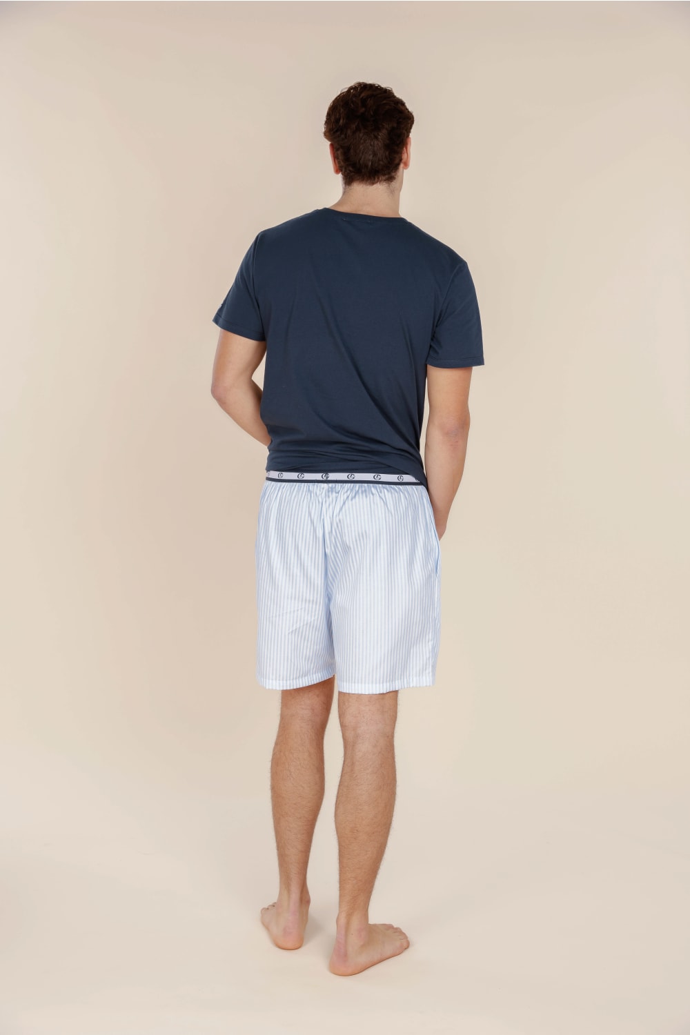 Man wearing navy t-shirt and light blue shorts on a beige background
