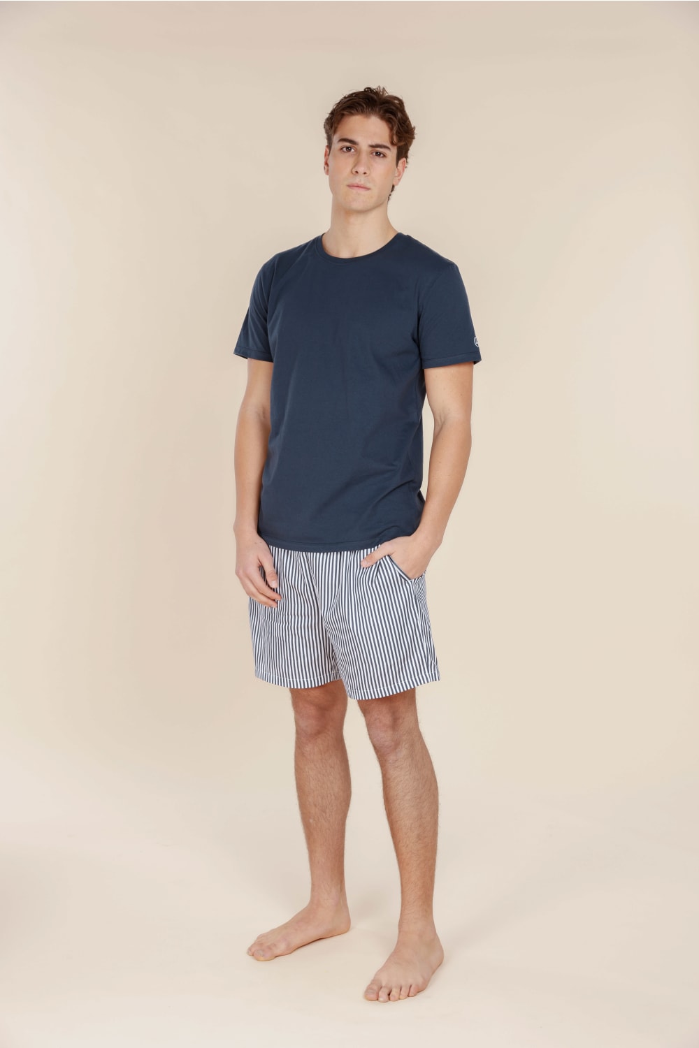 Man wearing a navy t-shirt and striped shorts on a beige background
